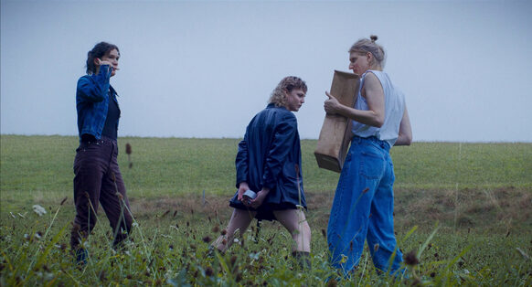Drei Frauen stehen auf einem Acker, eine Frau trägt eine Holzkiste